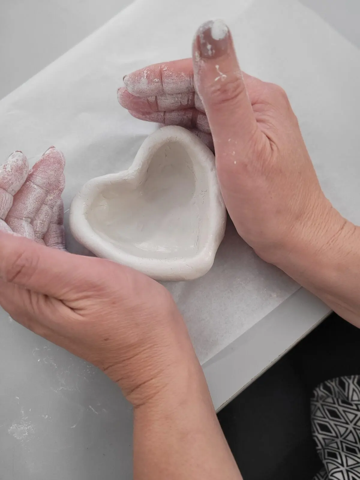 Two hands shaping a small white clay bowl on a workbench