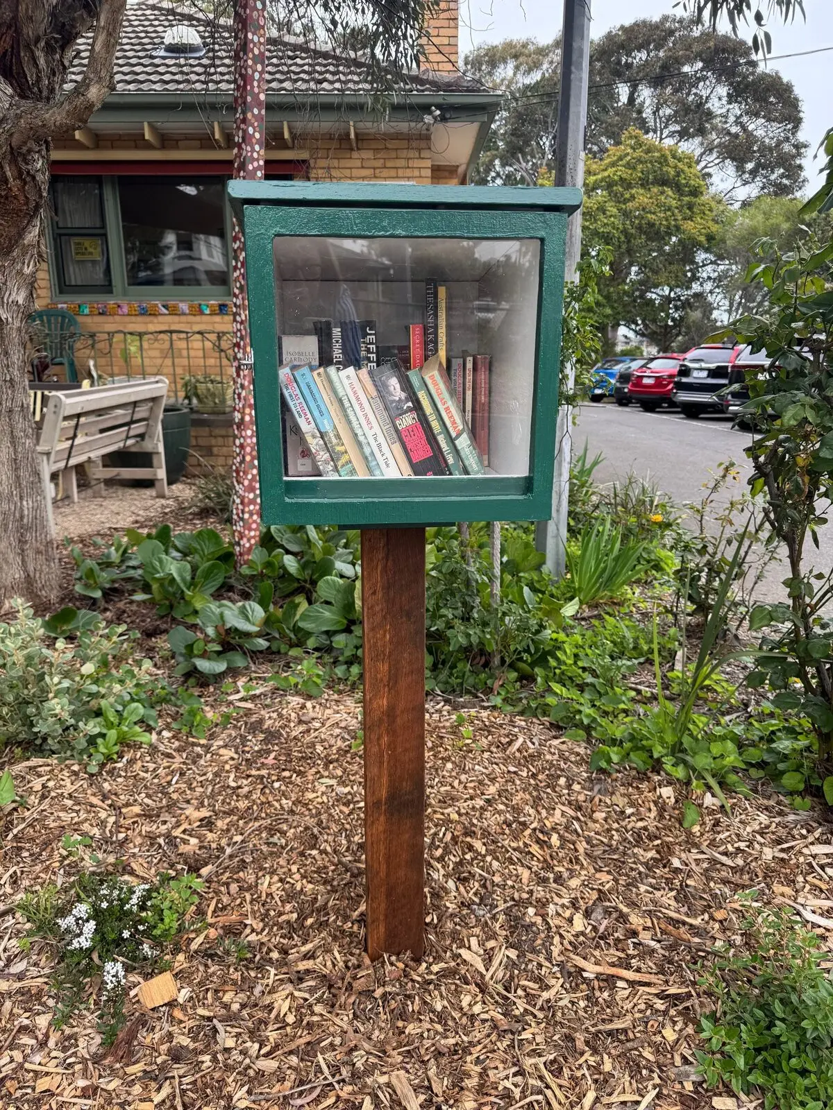 The little library box on its post in the front garden, its glass door showing a shelf of books, with the House behind