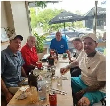 Men sitting around a long table over lunch, talking, with the garden through the window behind