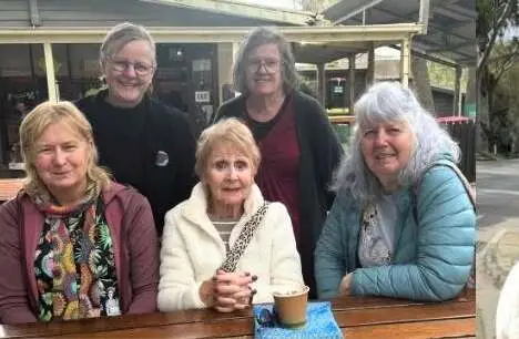 Five people gathered around a table outside a cafe with coffees