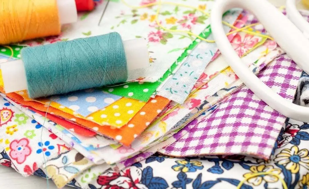 Reels of cotton in bright colours resting on a pile of patterned fabric