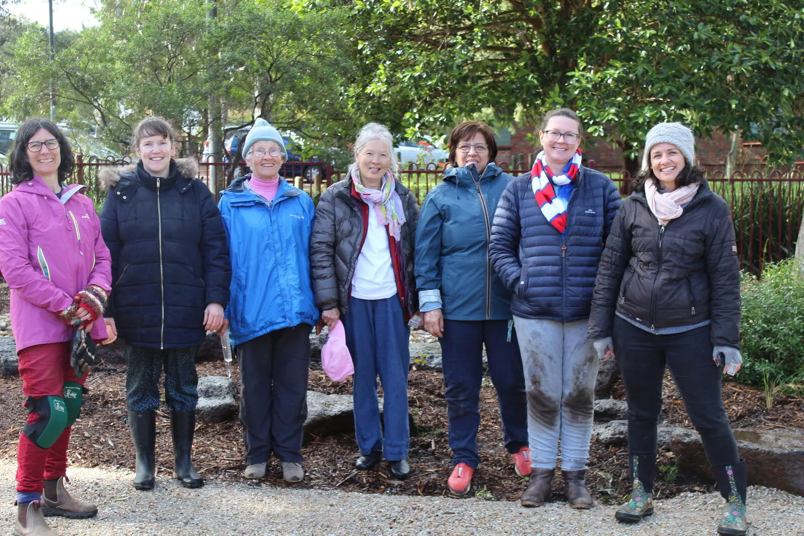 Seven people in winter coats and walking boots standing together on a woodchip path