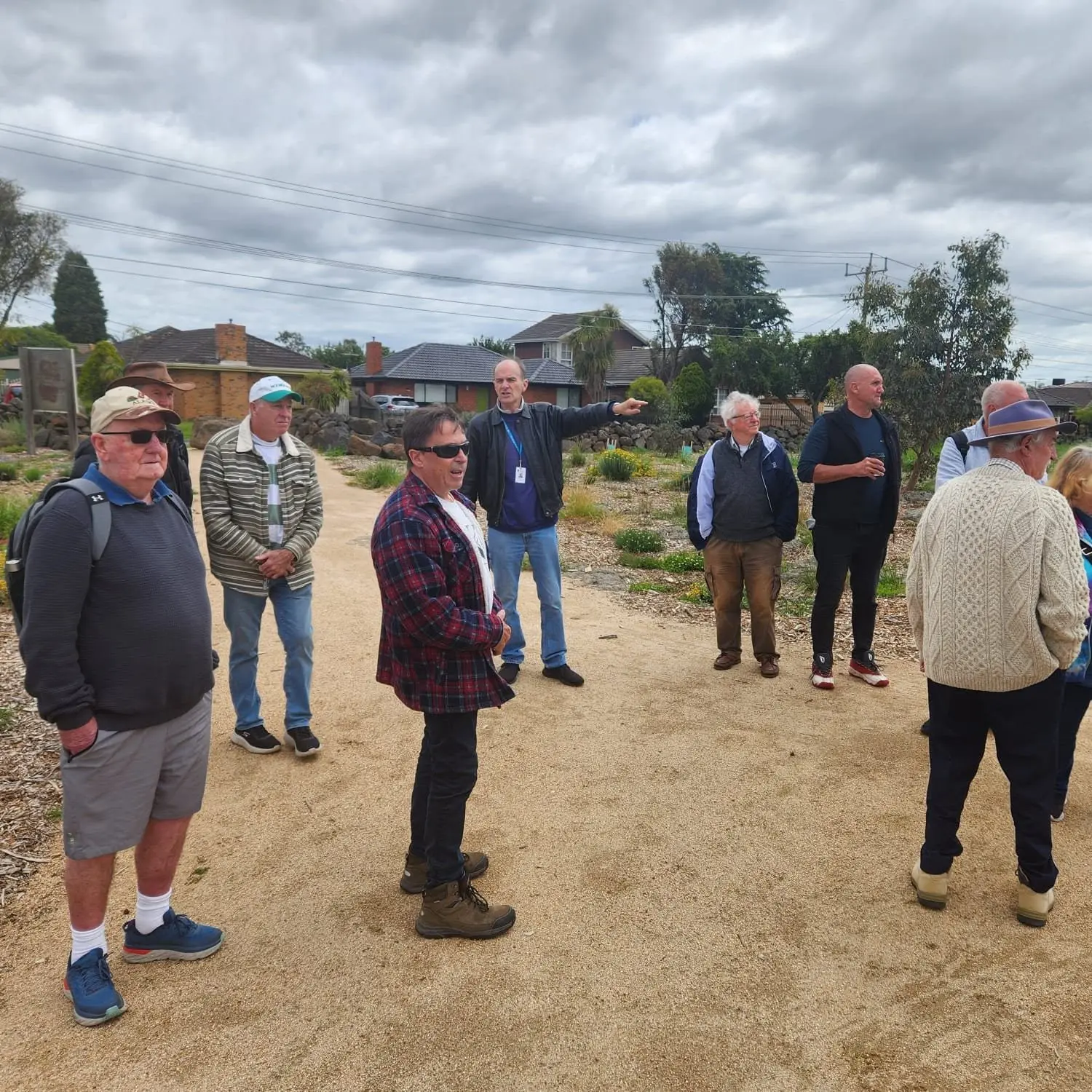 A group of men standing and talking on a gravel path at a heritage farm site, under a grey sky